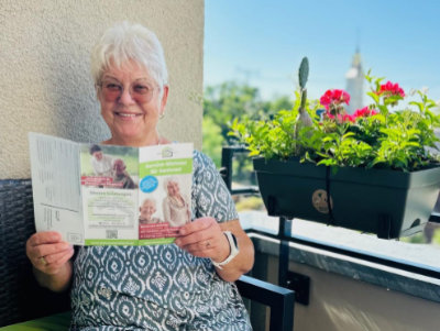 Eine ältere Dame sitzt auf ihrem Balkon und liest eine Broschüre